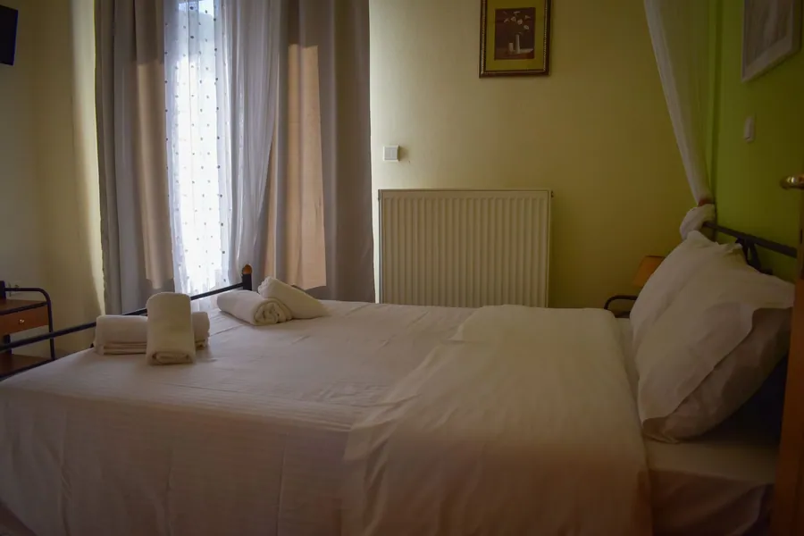 Διπλό κρεβάτι με λευκά σεντόνια δίπλα στο παράθυρο